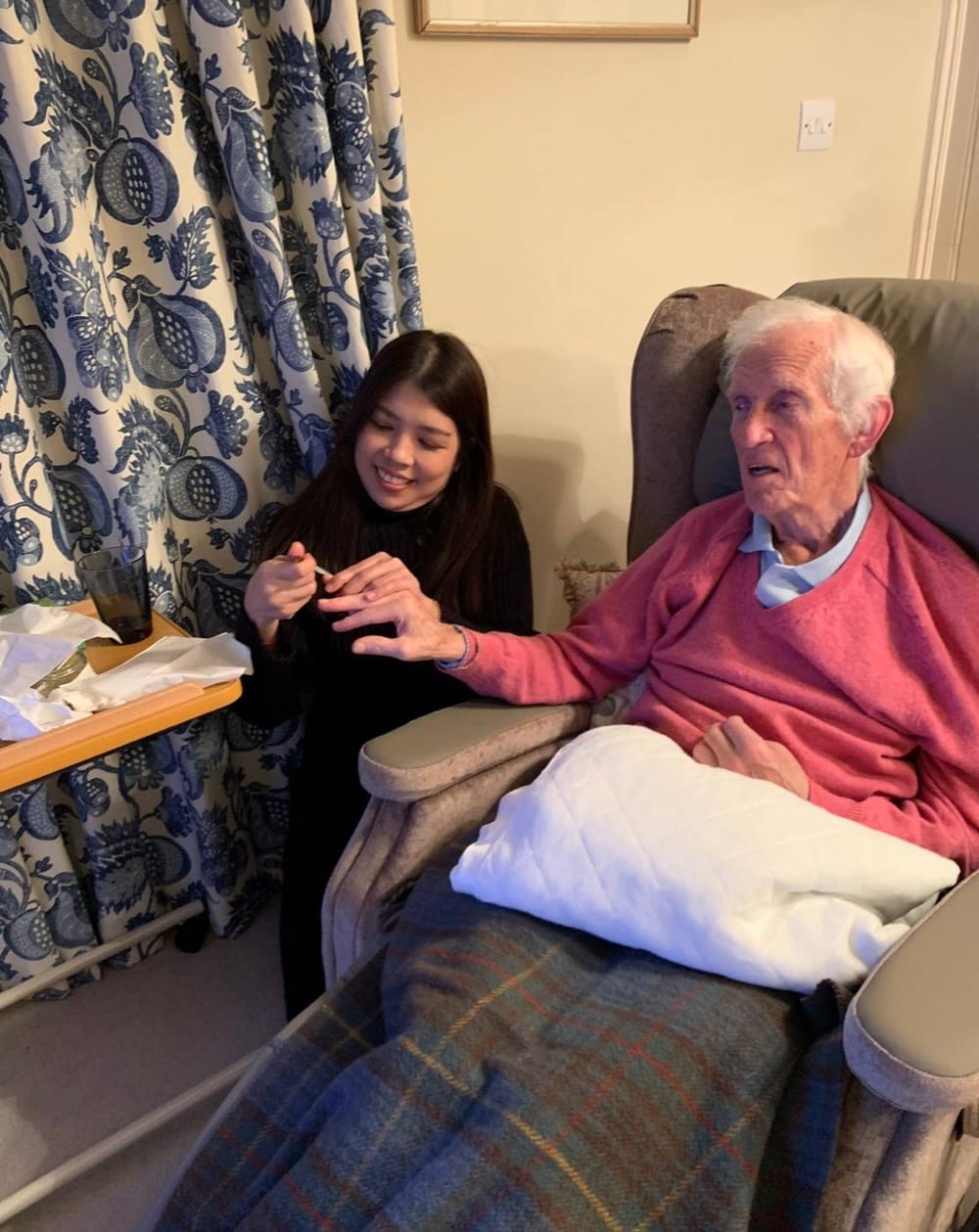 An Otter Care Professional painting a client's nails in his own front room, both of them smiling.