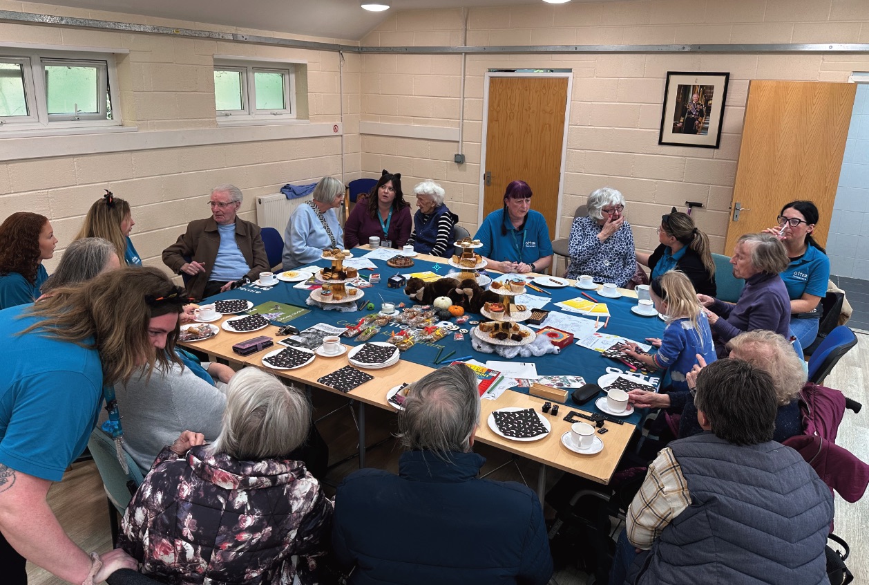 Clients and carers gathered around the table for tea and cake at the Otter Café
