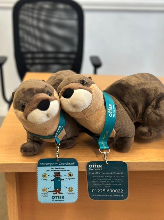 Two Otter soft toys wearing branded lanyards with a card carrying the emergency number